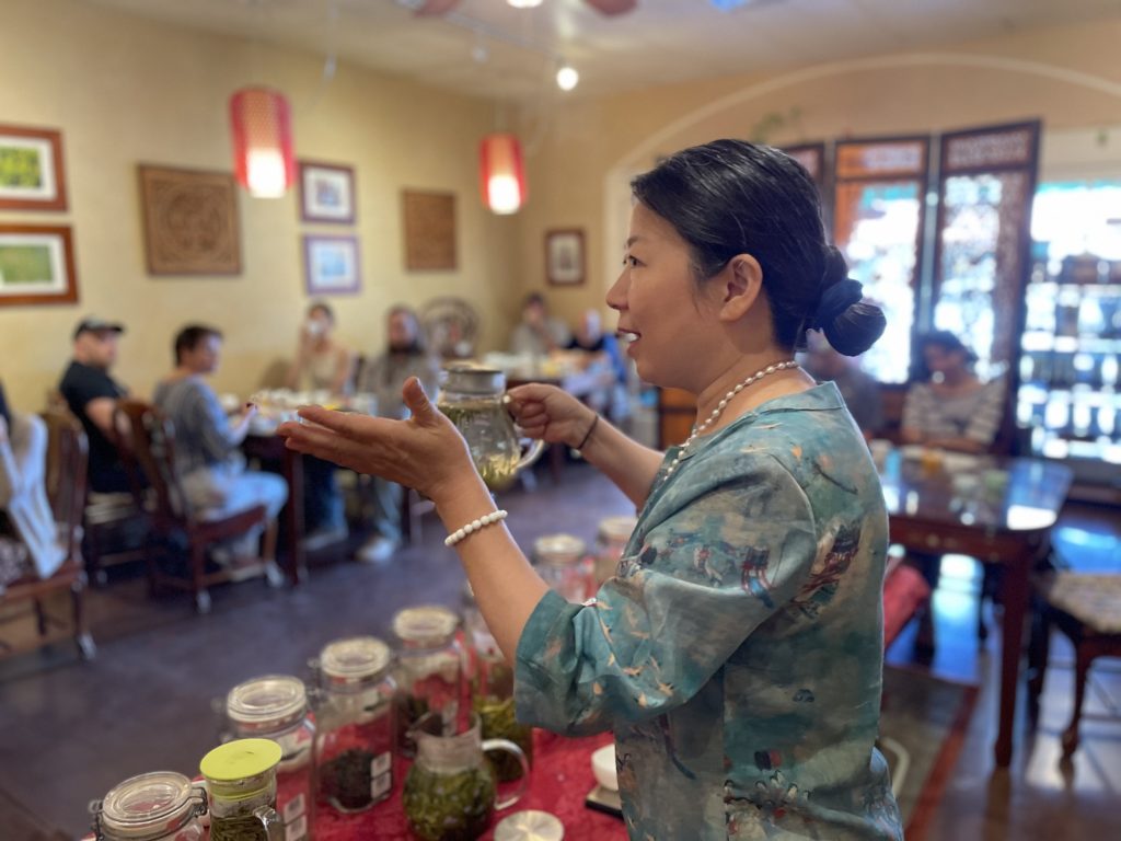 A woman speaking to a group of guests in a teahouse.
