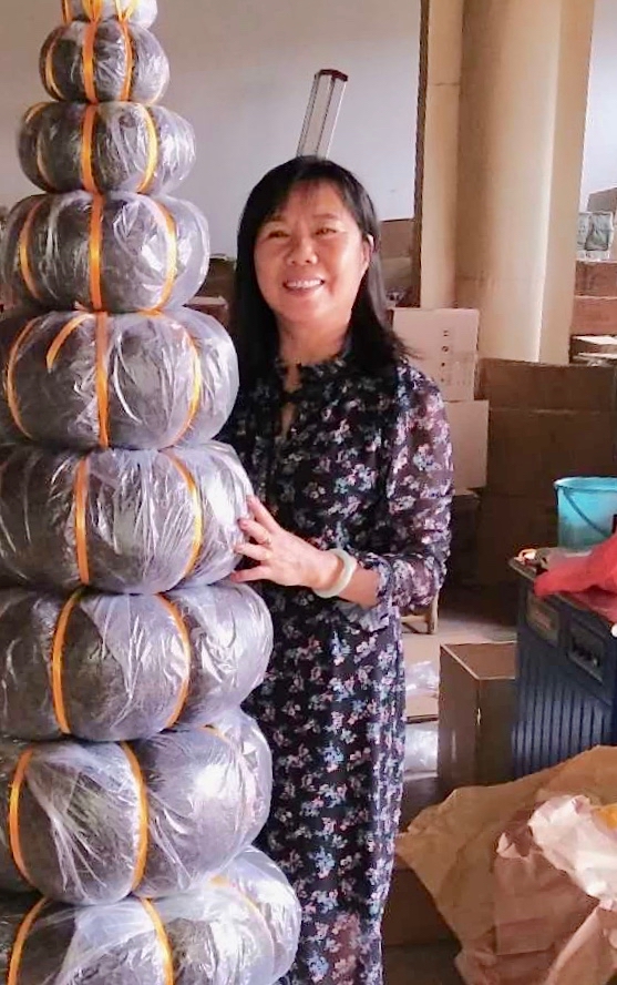 A smiling woman standing next to a tower of melon shaped puer cakes taller than she is.