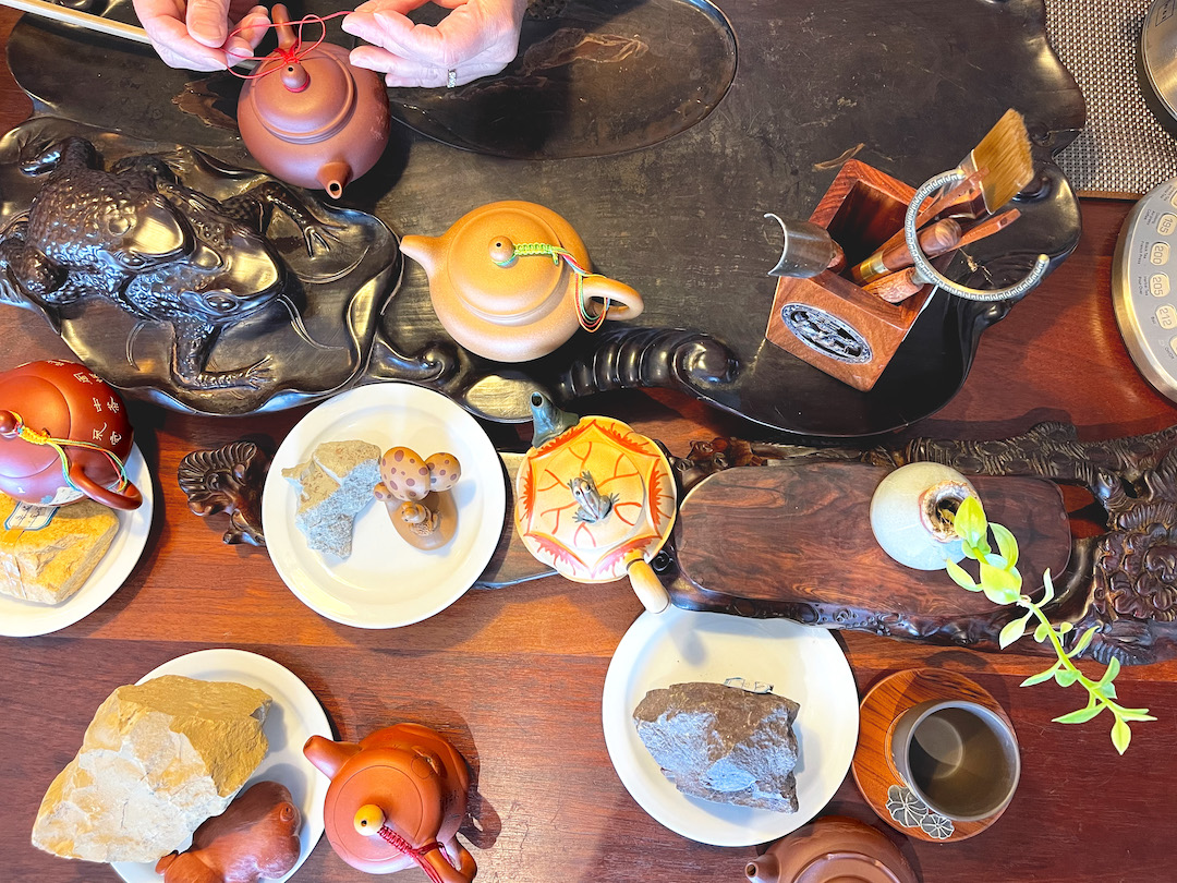 Above view of lots of yixing teapots and tea accessories laid out on a wooden table and tea table.