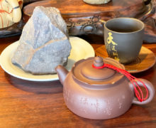 A purplish rock on a plate, next to a sculpted yixing teapot and clay teacup.