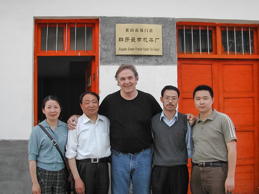 Five people standing in front of the red doors of a tea factory in Qimen.