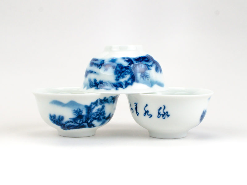 Small Wide Mouth Porcelain Landscape Teacups, one stacked upside down on two others.