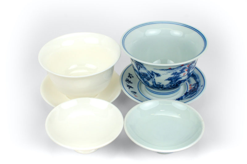 The palest blue base color of the Jingdezhen Shanshui Porcelain Gaiwan next to the warm white of a White Suet Jade Gaiwan.