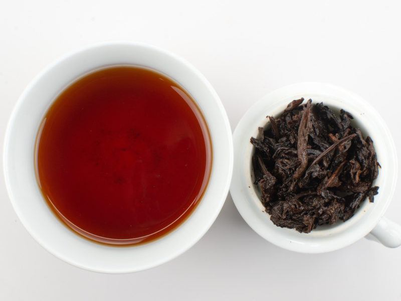 Cupped infusion of Yi Ban Xin Xiang (Flower Petal) shu puer tea and strained leaves.