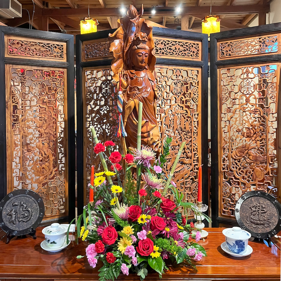A wooden statue of Guanyin and a large bouquet in front of an intricately carved wooden divider in the teahouse.