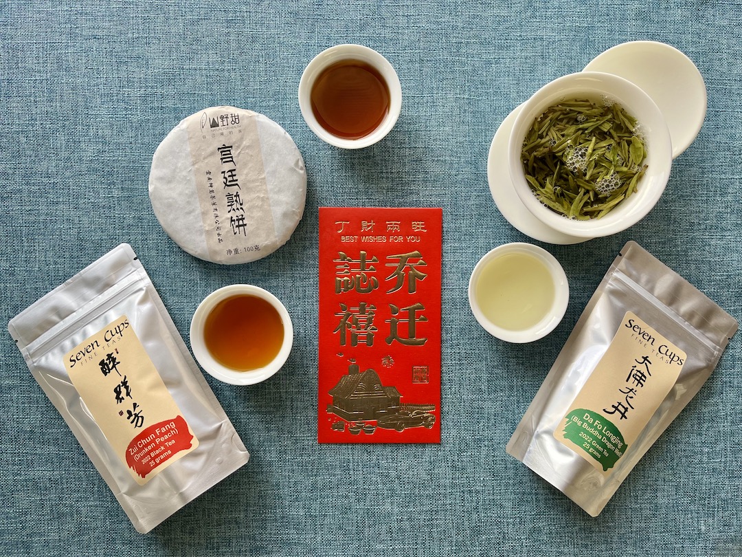 A spread of packaged tea, a gaiwan, and teacups on a blue cloth around a gold-embossed red envelope.
