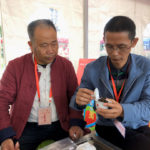 Two men sitting down together looking at a gaiwan full of rock wulong tea leaves.