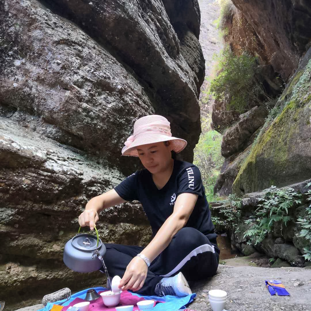 A woman seated in a stony mountain ravine brewing tea on a rock.