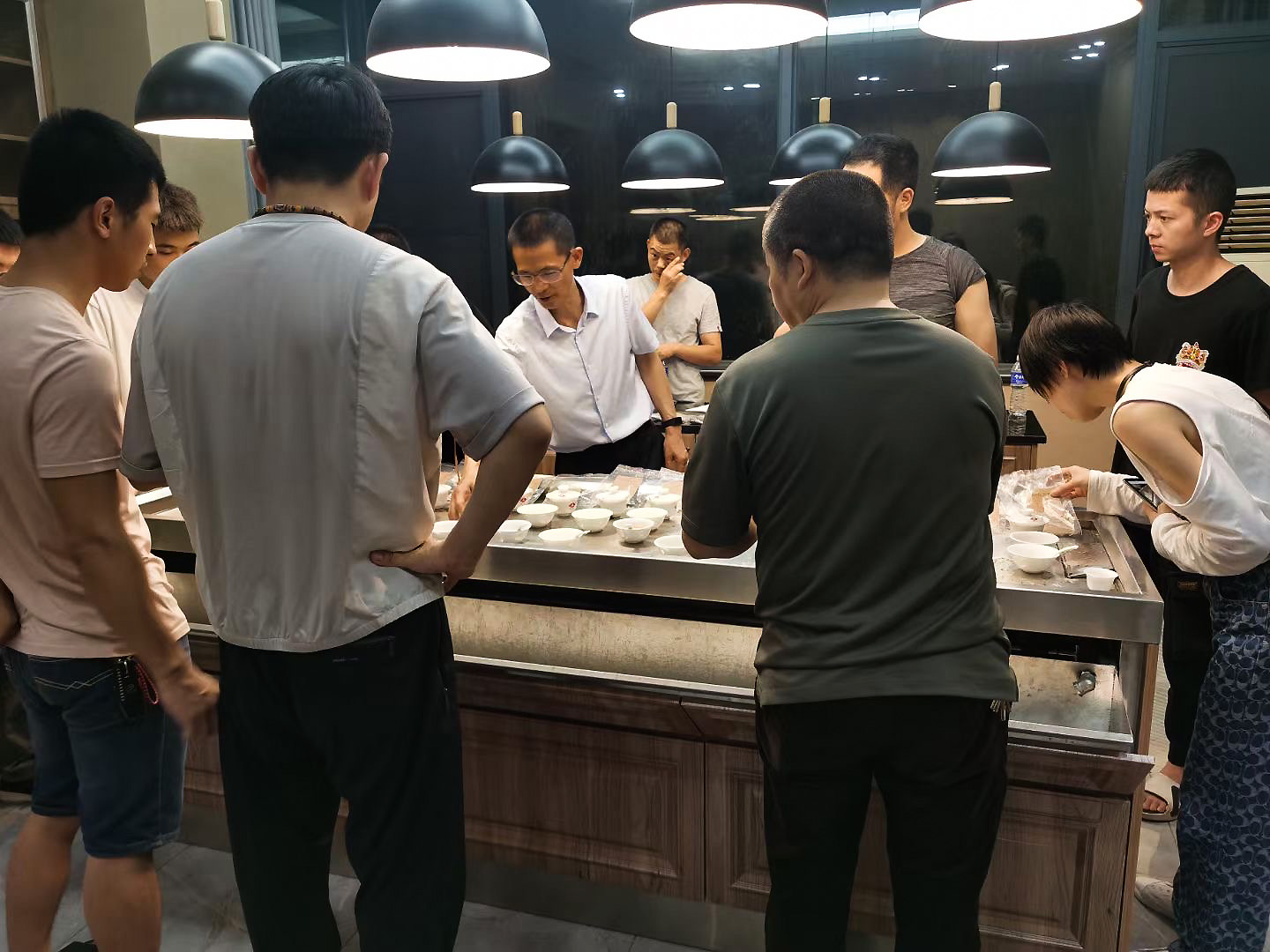 Several people gathered around a tea table covered in dozens of gaiwan.