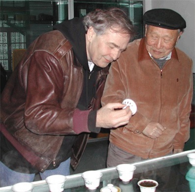 Two men next to a table with several gaiwan brewing rock wulong, inspecting a gaiwan lid together.