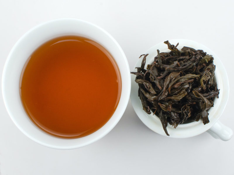 Cupped infusion of Qi Dan (Rare Crimson) rock wulong tea and strained leaves.