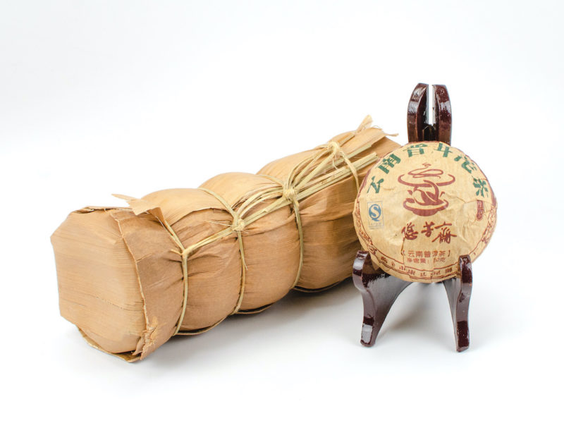 A tong of stacked Xiao Jinggua (Little Golden Melon) sheng puer tuocha wrapped in bamboo.