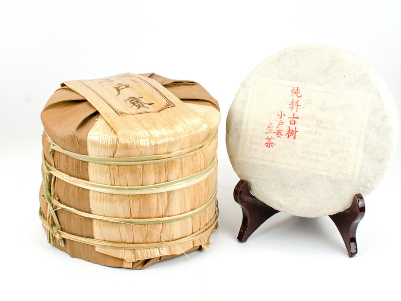 A tong of stacked Xiaohuzhai Sheng Puer cakes wrapped in bamboo.