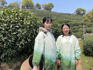Two women in white and green ponchos stand in a tea field.