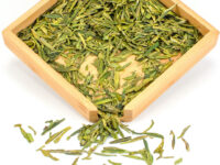Late Spring Heirloom Da Fo Longjing green tea dry leaves in a wooden display box.