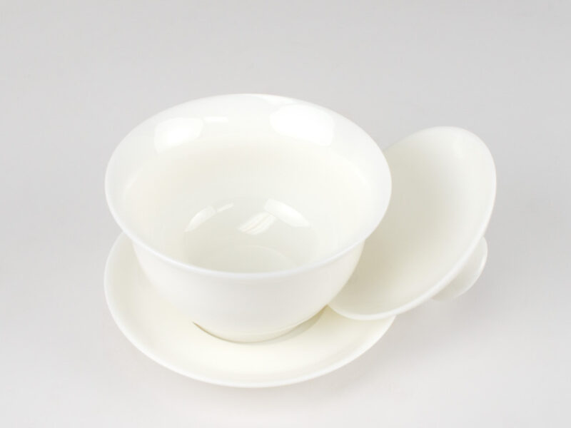 A white porcelain gaiwan with its lid opened and resting on its side.