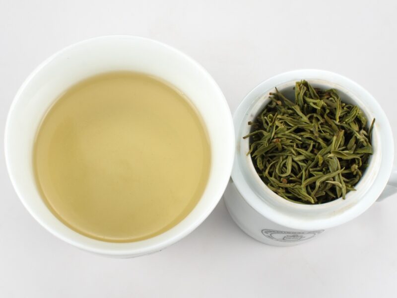 Cupped infusion of Mengding Yu Lu (Jade Dew) green tea and strained leaves.