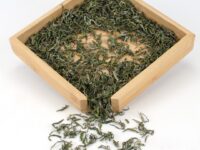 Ming Qian Mogan Green tea dry leaves displayed on a bamboo tray.