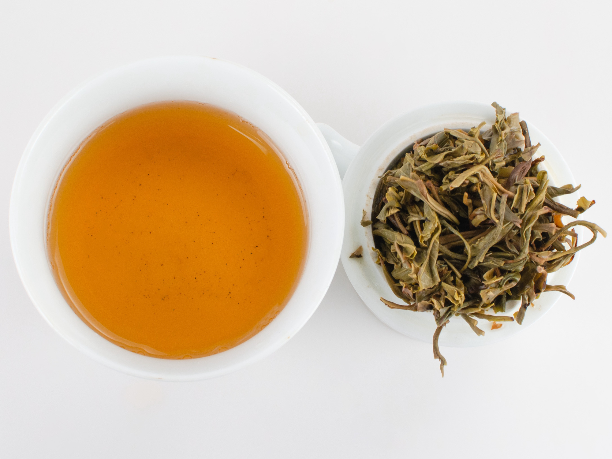 Cupped infusion of Youle Huangshancha (Youle Forest Tea) sheng puer tea and strained leaves.