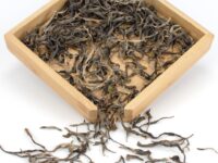 Naka sheng puer tea dry leaves in a wooden display box.