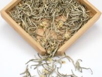 Moli Yinzhen (Jasmine Needle) scented green tea dry leaves and jasmine flowers in a wooden display box.