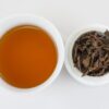 Cupped infusion of Yiwu Sun-Dried Yunnan black tea and strained leaves.