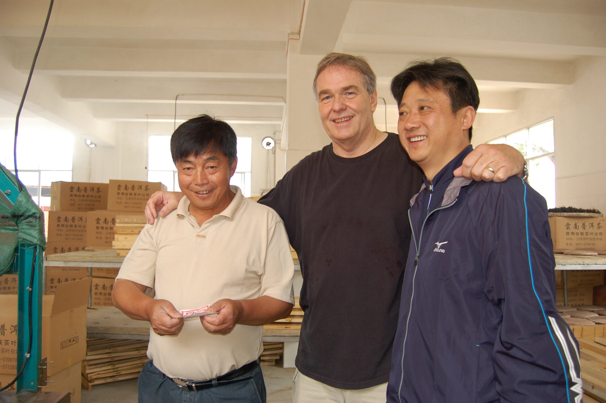 3 men standing together, smiling, in a puer compressing factory in Yunnan province