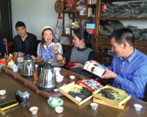 4 people sitting at a tea table exchaning gifts. 