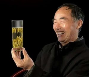Tea maker holding a tall glass cup of Junshan Yinzhen. The steeping tea has turned vertically as they sink to the bottom.